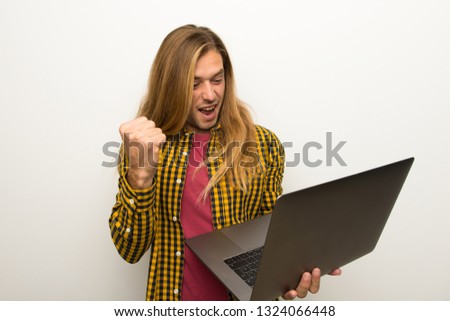 Blond man with long hair and with checkered shirt with laptop and celebrating a victory