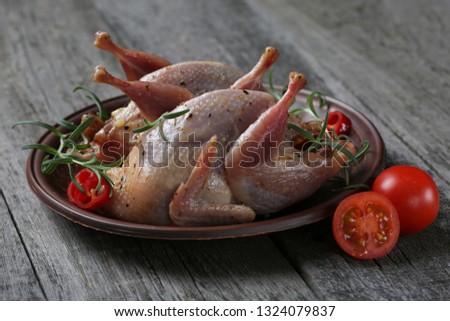Raw quails ready for cooking on ceramic plate with spices on old wood background