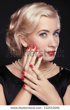 Blond woman with make up and red manicured nails over black, studio photo