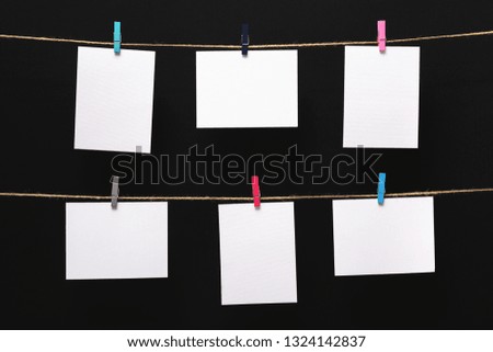 empty paper cards attached with colorful clothespins on linen rope on a black background, blank templates for images or text, concept office and photo industry, decor