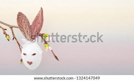 Easter egg with funny bunny ears,, eyes and lips and a blooming cherry branch isolated on a pastel background background