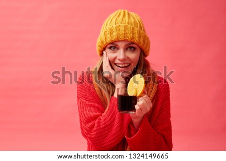 Woman in a red sweater and knitted hat holding a cup of hot mulled wine with an orange slice. Red background. Studio