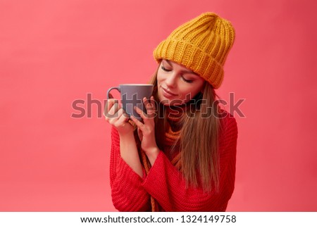 Beautiful woman in warm cozy sweater with cup of hot drink. Red background. Studio