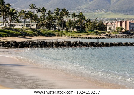 clear blue water, small waves on shore. In the background low level buildings and a town in the distance, sunny day.