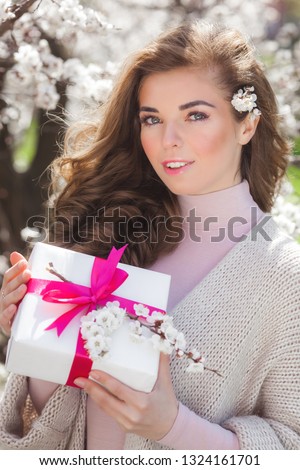Attractive young woman holding present box. Female on spring background with gift. Beautiful lady outdoor.