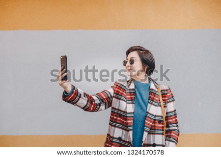 Portrait of pretty young woman taking a selfie with mobile phone, wearing fancy clothes and posing for her online followers in front of a multicolored background. Space for copy, text, advertising.