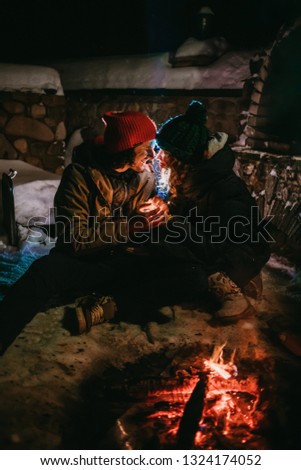 Pretty couple in colored hats sitting near the fire.