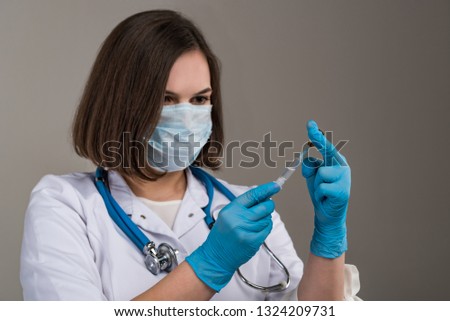 Young attractive nurse with mask fills in syringe in her hand close