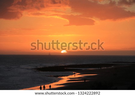 A group of people walk on the beach at sunset.