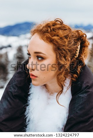 A charming girl with wavy hair sits against the background of snowy mountains