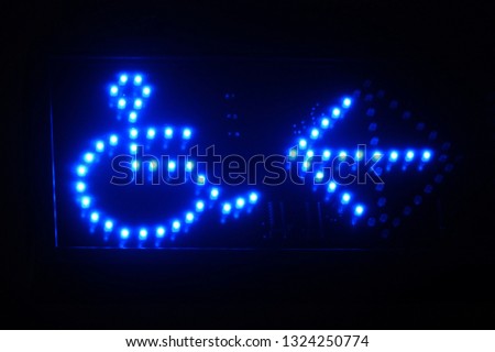 Illuminated blue led signage indication - pointing to were the disability access is. Arrow and person in wheel chair icons.