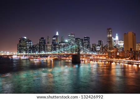 New York City Brooklyn Bridge and Manhattan skyline with skyscrapers over Hudson River illuminated with lights at dusk after sunset.