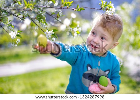 Little beautiful boy  holding colorful Easter eggs.  child walks against background of flowering gardens. Cherry branches behind boy.  happy child gathered eggs from Easter 
