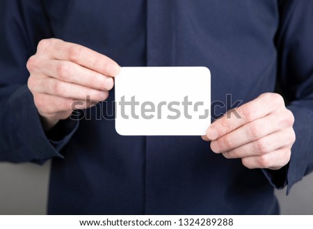 A man in a blue shirt holding a white business card