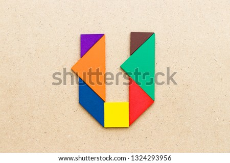 Tangram puzzle in alphabet letter U shape on wood background