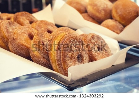 Closeup of several freshly baked warm Cronuts sitting in pans on a glass display at a French pastry shop