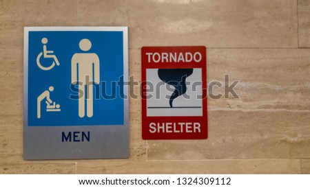 Sign of a tornado shelter next to a sign of a men's restroom