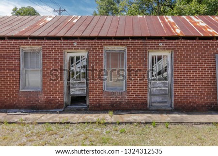 Blue skies, rusted tin roof, shattered wooden doors and red brick walls of an abandoned motel in the deep south