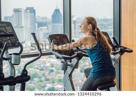 Young woman on a stationary bike in a gym on a big city background