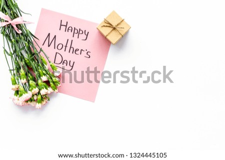 Happy Mother's Day concept. Hand lettering near bouquet of pink carnation and gift box on white background top view copy space