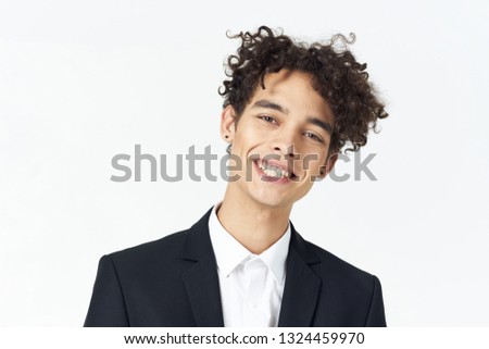 Curly guy in a shirt and jacket is smiling at the camera, cropped look                          