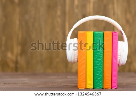 Multicolored books with white  headphones on wooden background. Empty space for text
