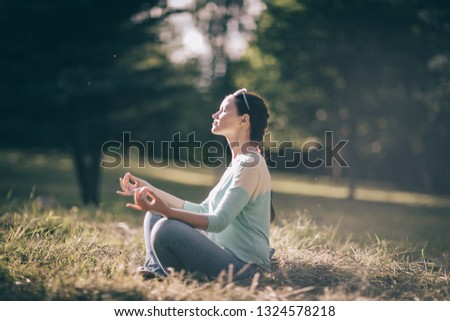 beautiful young woman meditating in Lotus position sitting on the lawn.