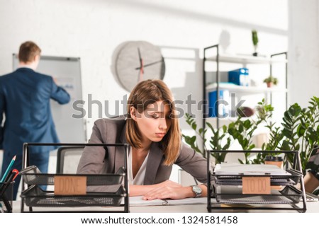 selective focus of sleepy businesswoman sitting at desk near document trays with lettering, procrastination concept