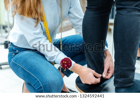 Alterations tailor measuring trousers on a customer, close-up Royalty-Free Stock Photo #1324592441