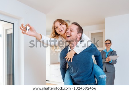 Man carrying his wife piggyback who is showing the house keys being happy