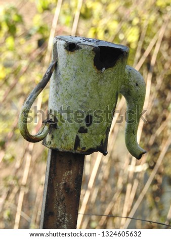 Isolated antique rusty metal teapot impaled upside down on a metal bar with a yard or garden plants and vegetation bokeh as background. Teatime, decay concept
