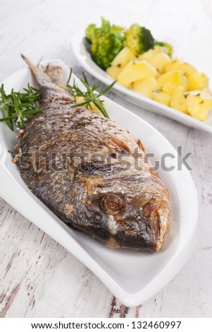 Grilled fish on plate, steamed vegetable in background. Culinary mediterranean seafood eating concept.