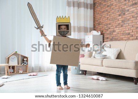 Cute little boy playing cardboard armor in living room Royalty-Free Stock Photo #1324610087