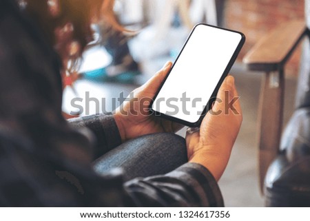 Mockup image of hands holding black mobile phone with blank white desktop screen in cafe