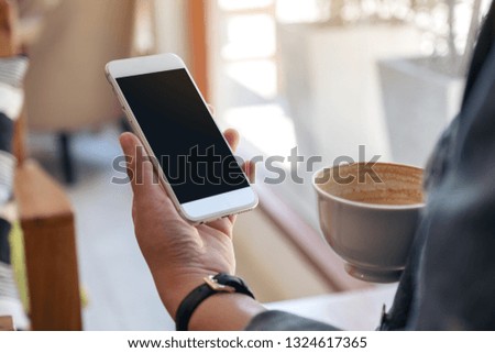 Mockup image of hands holding white mobile phone with blank screen while drinking coffee 