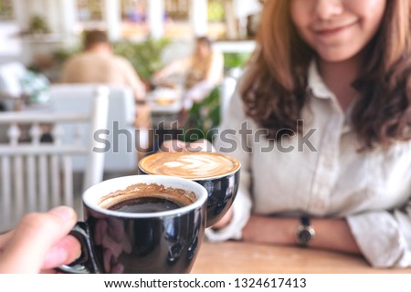 Close up image of a woman clinking coffee mugs to a man in cafe