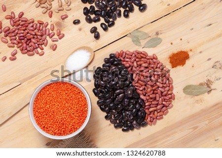Assortment of grains of red and black bean, lentil on a wooden background. The photo depicts a still life on a wooden table made of beans, lentils, bay leaf, salt on a spoon, red pepper. Top view.