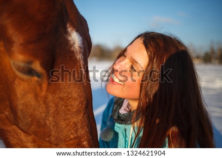 Head of a horse and a girl's hands close up. She feeds the red horse.