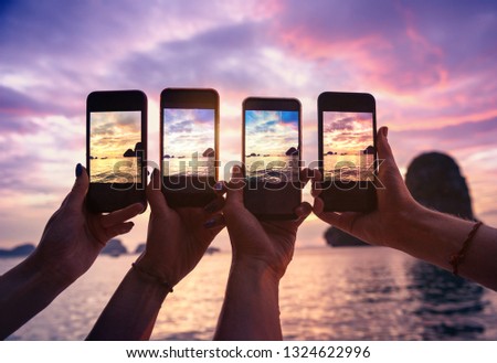 Closeup photo of four hands with mobile phones taking photo of beautiful sunset over sea bay