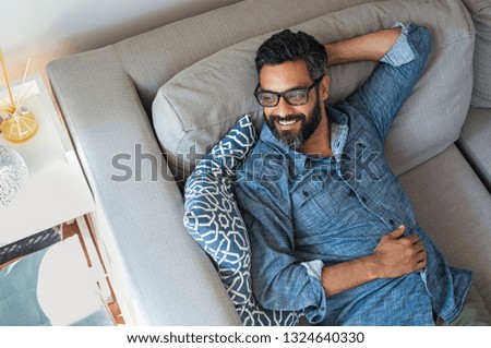 Mature man resting on sofa and thinking about the future. Hispanic man lying on couch and looking away. Smiling casual guy relaxing and daydreaming on sofa at home. Royalty-Free Stock Photo #1324640330