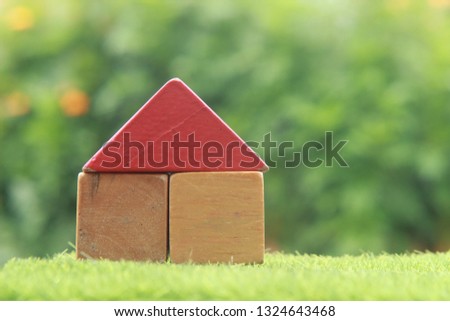 Red Top House from Wooden Block Toy at Fresh Green Grass for Sale or rent with blur Tree and Yellow Flower 
