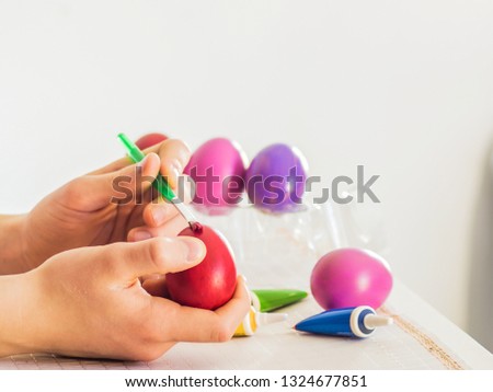 Easter egg coloring process with a brush of acrylic paints, hand action on a white table on a white background of the room