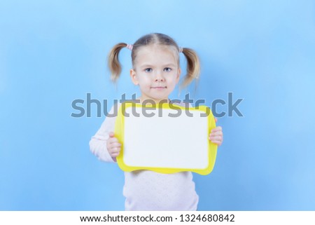 A little girl with a hair two tails. A cute child with blond hair is holding a sign with space for text. Bright photo with copy space.