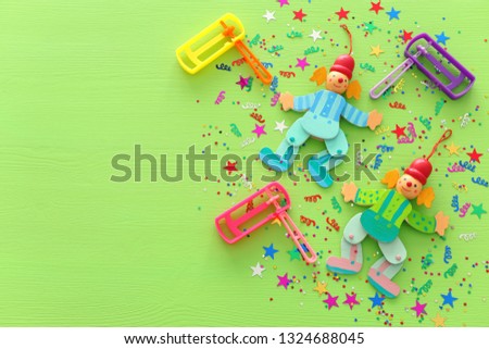 Purim celebration concept (jewish carnival holiday), clowns, confetti and noisemaker over wooden green background