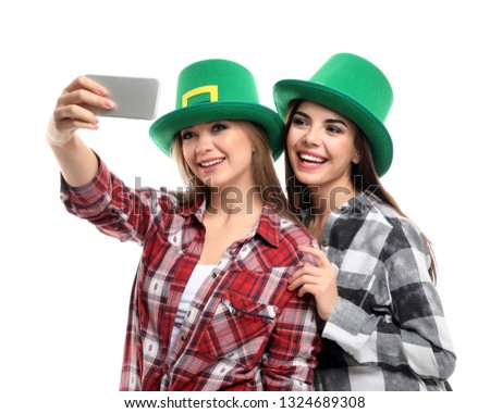 Beautiful young women in green hats taking selfie on white background. St. Patrick's Day celebration