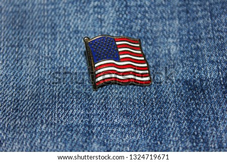 American flag isolated on blue denim jeans. Small pin of United States of America national flag on top of classic denim jeans texture background. Clothing industry and brand apparel in America concept