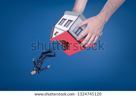 Close-up of man's hands holding house with hole in roof upside down and dropping out little businessman. Real estate scam. Eviction of tenant. Housing issues. Royalty-Free Stock Photo #1324745120
