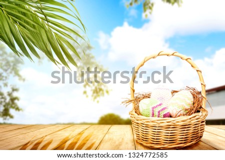Colorful easter eggs on nest in wooden basket on the wooden table with palm branches and trees with blue sky background. Happy Easter