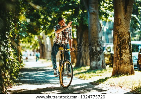 A handsome young man goes to the city ride with his bike, sitting on it and waving to someone.