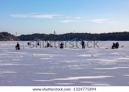 Ice fishing in Naantali, Finland. Sunny winter day with bright blue sky.